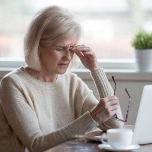 Older woman with eye ache holding glasses